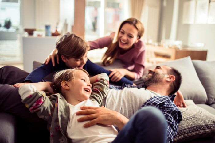 happy cohabiting family with two parents and two children laughing on sofa